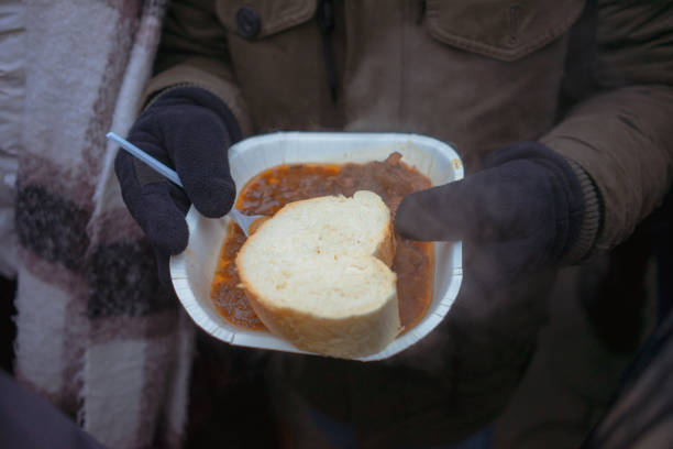 A piece of bread and stew in the hands of a man in winter outside, close-up view.