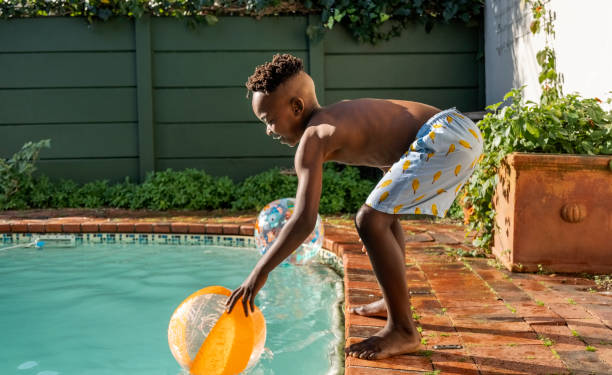 istock Little African boy playing with ball on pool edge 2200220249