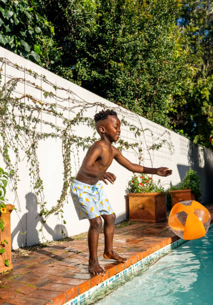 istock African boy standing on pool edge playing with ball 2200220447