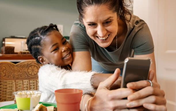 istock Mother and adopted daughter smiling at dining table with mobile phone 2200220611