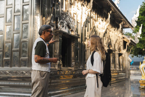 A senior tour guide showing a foreign tourist the Buddha statue while explaining symbolism and craftsmanship