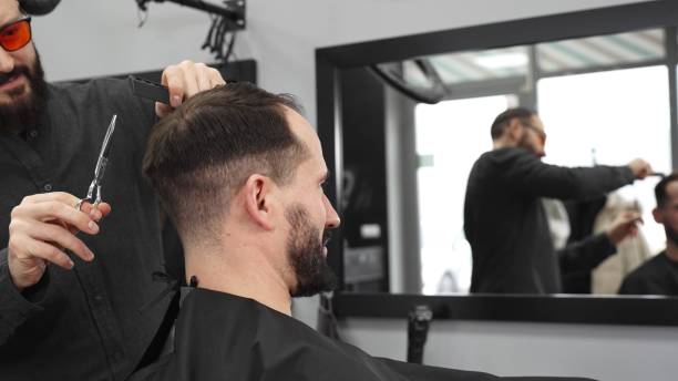 istock Skilled barber working on male client's hairstyle, carefully combing and preparing precision cut in contemporary barbershop setting 2200223258
