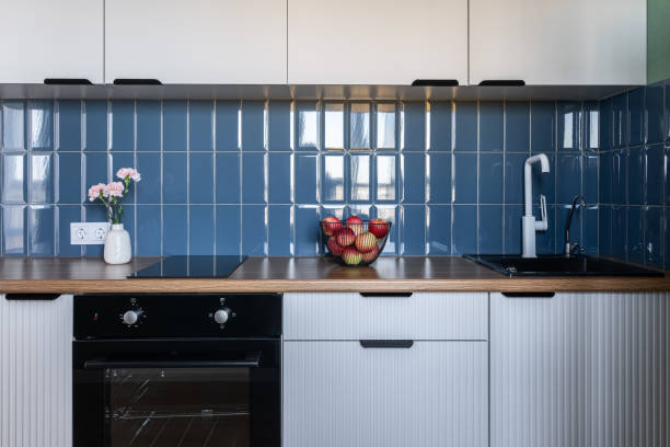 istock design of modern small kitchen. built-in kitchen with white cabinets, blue tile backsplash, wooden countertop. white kitchen unit. oven, flowers on vase, white faucet 2200225046