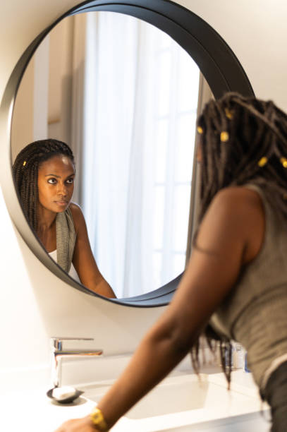 istock Young woman looking at herself in bathroom mirror 2200226158