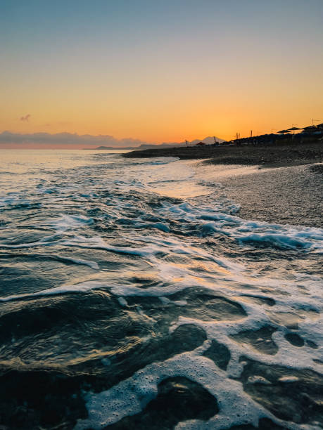 istock Soft waves lapping rocky shoreline during vibrant sunset along Cretan coastline, capturing serene Mediterranean summer evening atmosphere 2200227550