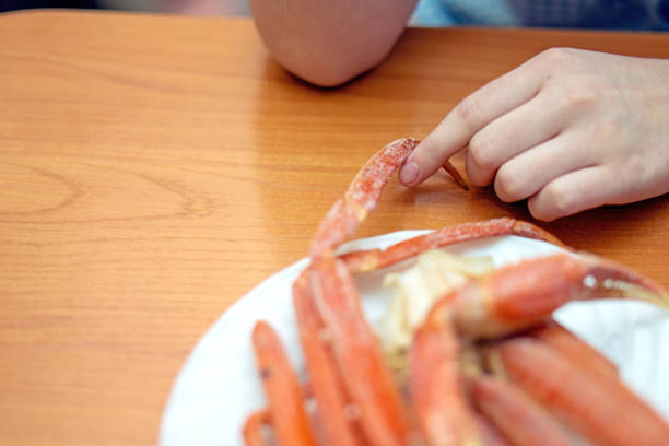 child's hand playfully touches a cooked crab claw on a table, showcasing curiosity and exploration of food textures. This image captures the essence of childhood wonder and culinary discovery