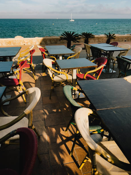 istock Seaside restaurant terrace featuring empty tables, vibrant chairs, sailboat gliding across blue horizon with calm ocean backdrop 2200227882