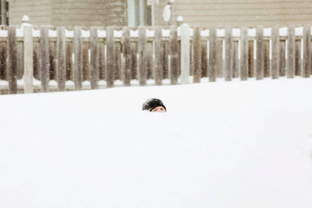 A man is walking down a road, past a very high snowbank.
