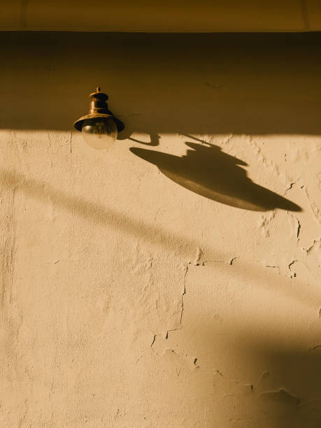 istock Vintage lamp casting long shadows across weathered wall, golden sunlight illuminating rustic surface during warm late afternoon light 2200228569