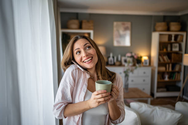 istock A young woman is smiling while holding a green cup and using her mobile phone, radiating happiness and relaxation in a cozy home environment 2200229349