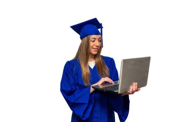 istock Young graduate student using laptop wearing blue gown and graduation cap 2200232416