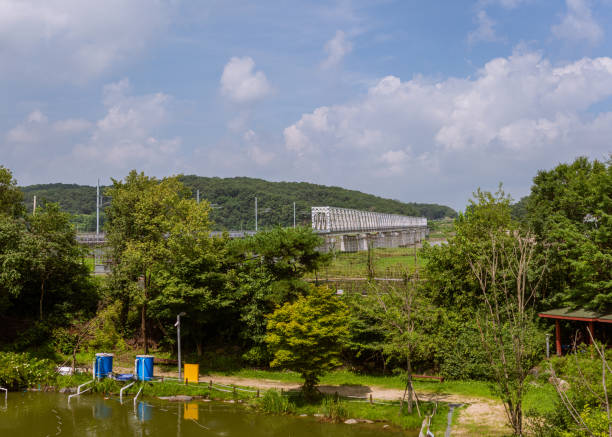 istock Steel Railway Bridge Spanning Green Landscape With Reflective Pond And Rolling Hills Under Bright Blue Sky 2200233150