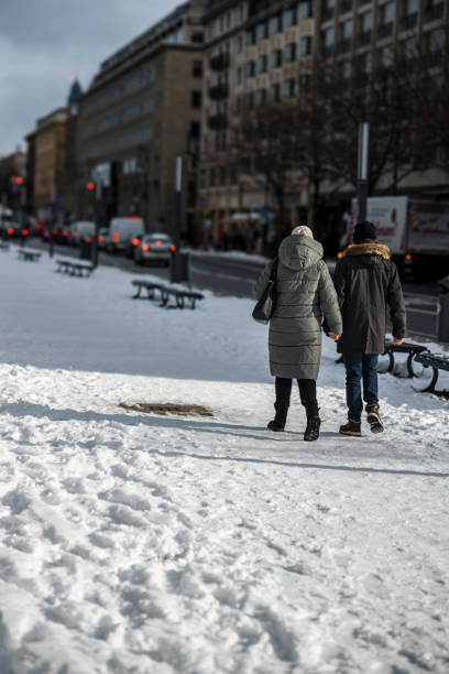 Visitors walk hand in hand along Unter den Linden in Berlin, enjoying a winter day. Snow blankets the ground, creating a serene atmosphere in the bustling city.