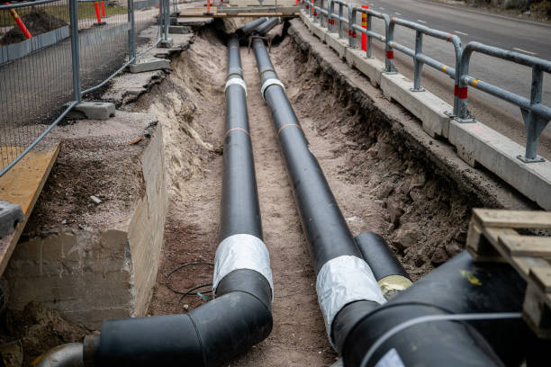 istock Large black underground pipes being installed in an excavated trench at a construction site, surrounded by dirt and gravel, with safety barriers 2200244590