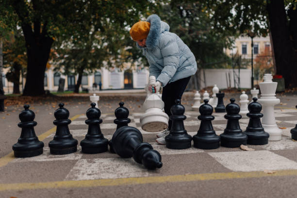 istock Girl playing giant chess in city park makes checkmate move 2200245457