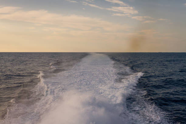Endless ocean horizon with a foamy white wake trail extending into the distance under a pastel-colored sunset sky creating a peaceful and reflective maritime scene. Captured in eastern sea between Busan, South Korea and Fukuoka, Japan, Asia