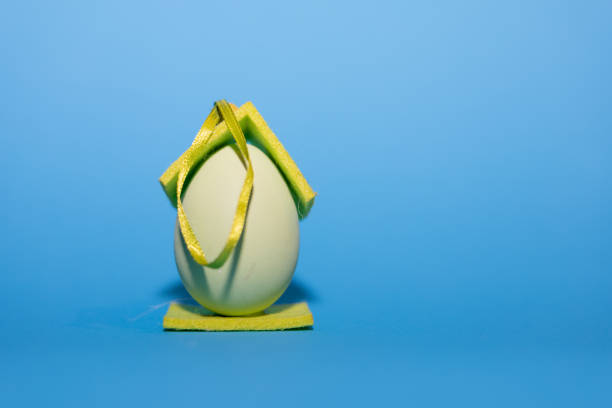 A small toy chicken inside an egg-shaped house, pecking at grain, on a blue background. High quality photo