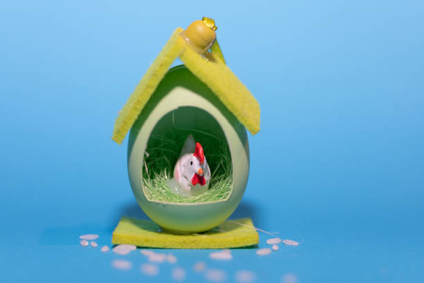 A small toy chicken inside an egg-shaped house, pecking at grain, on a blue background. High quality photo