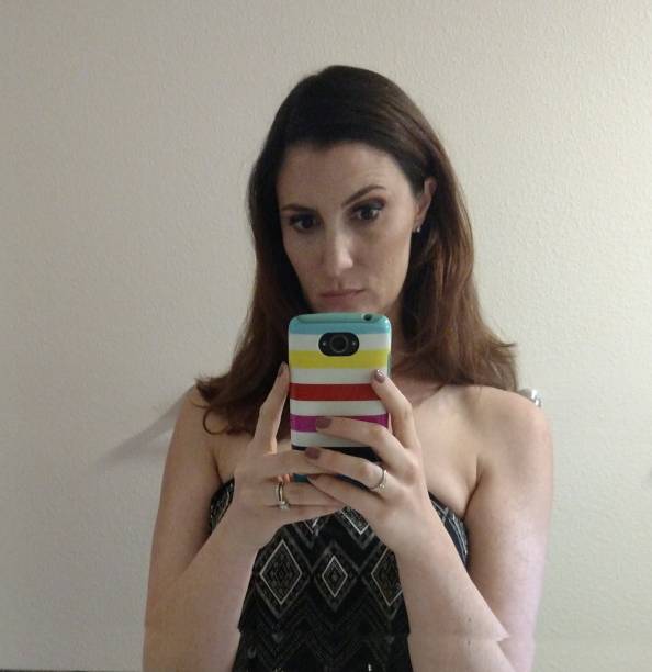 Medium closeup of a dark haired woman talking a mirror selfie in a strapless brown and black dress