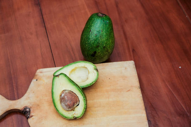 istock Halved avocado with pit and whole avocado on wooden cutting board 2200256697