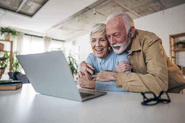 istock Happy senior couple embracing while using laptop at home 2200257559
