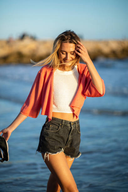 istock smiling young blond woman walking on beach by water 2200269999