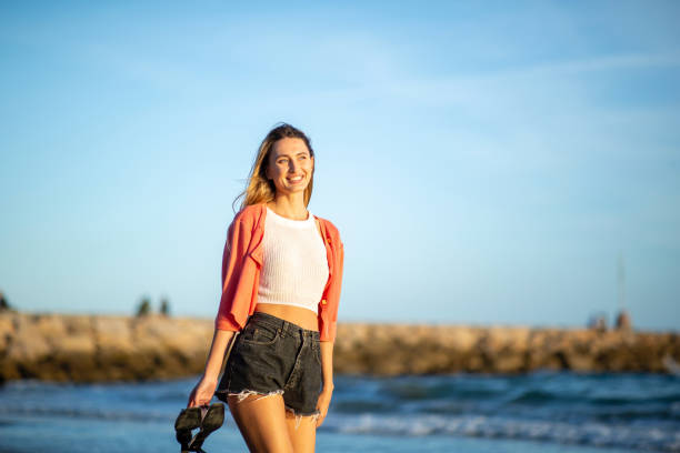 istock smiling young blond woman walking by beach 2200270006
