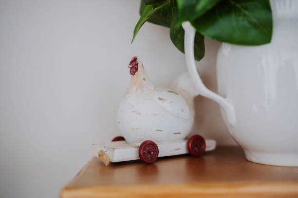 A wooden chicken on wheels sits on a shelf near a white ceramic pitcher.