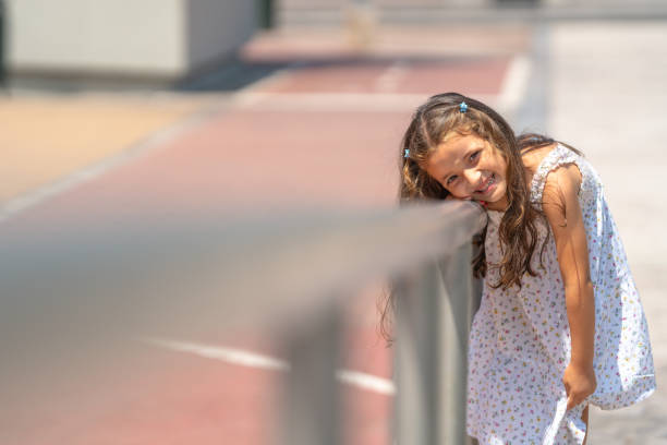 Portrait of a cheerful young girl leaning on a metal railing, enjoying a sunny day in a city environment