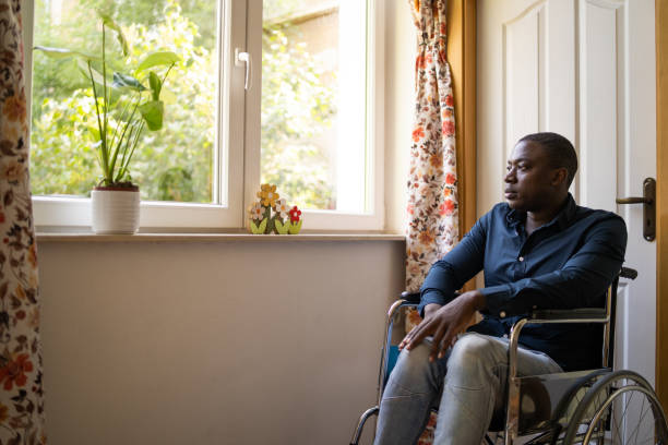 istock An African-American man looking through a window while sitting in a wheelchair 2200271595