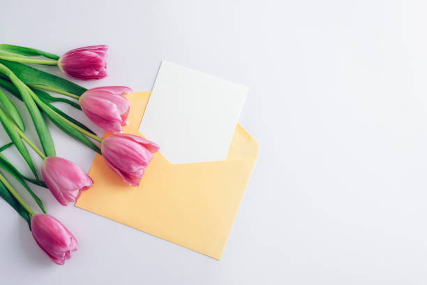 istock Yellow envelope with a blank white card and pink tulips on a white background. Spring holiday concept. Top view, flat lay, mockup 2200273142