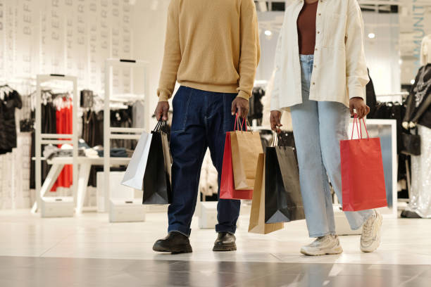 Modern shopping couple in casualwear carrying paperbags while walking along showroom with trendy apparel in the mall