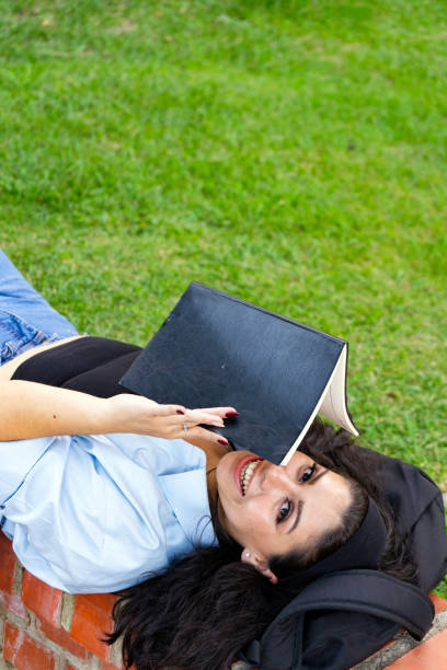 Latina young woman reading a book in the park, enjoying a peaceful moment in nature, high angle view.