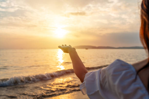 istock Young woman's hand reaching for the Sun during beautiful sunset at the tranquil beach 2200300935