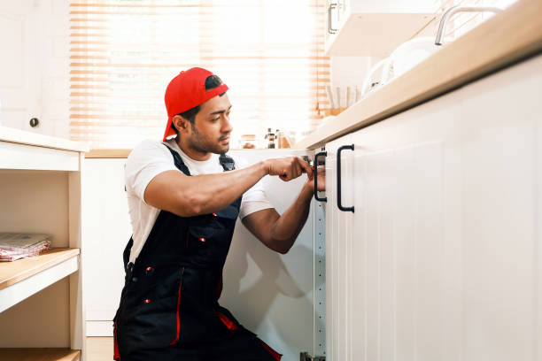 Professional handyman in uniform installing a kitchen cabinet handle. Home repair, renovation, and maintenance services concept. Skilled worker using a screwdriver for cabinet fitting.