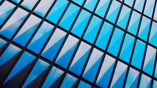 istock Geometric Reflections. An abstract close-up of a modern glass building facade, featuring a striking pattern of diagonal blue reflections framed by a black grid structure 2200319779
