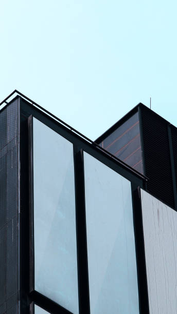 istock Minimalist Architecture. A modern building facade featuring sleek glass panels and geometric black frames against a pale sky 2200319782