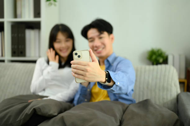 istock Happy couple relaxing on the sofa and using a smartphone to take a selfie or video call 2200320038
