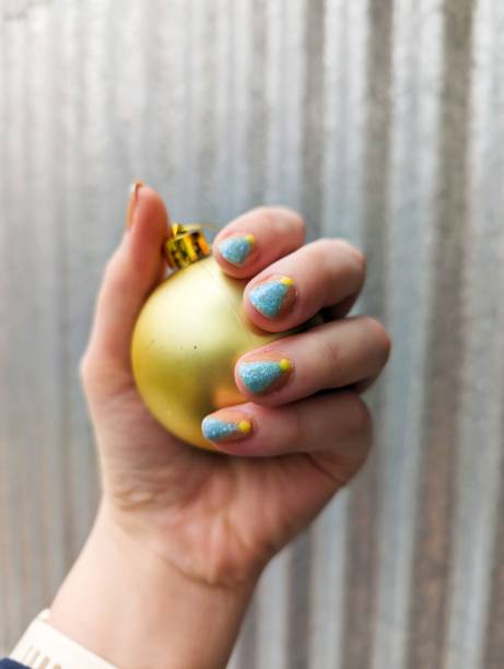 istock Hand with painted nails depicting Christmas trees holding a gold bauble 2200322976