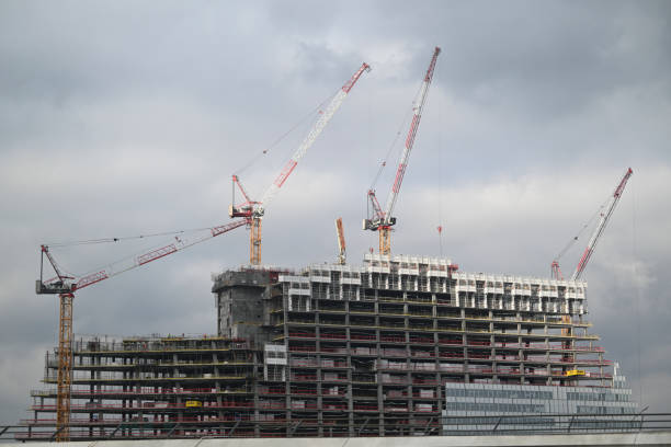Workers are busy on a construction site in Paris, where a high-rise building is taking shape under a cloudy sky with cranes lifting materials.