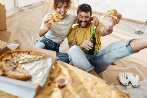 istock Cheerful couple having fun while eating pizza at their renovating apartment. 2200323720