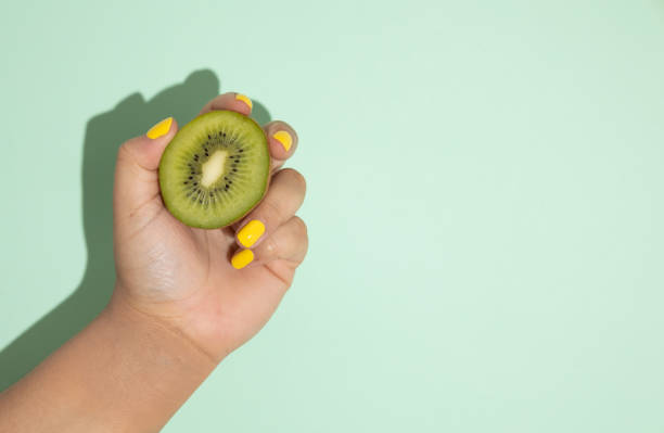 istock Female hand holding a kiwi on a light green background 2200323992