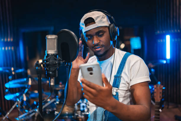 Young musician recording music in professional studio using smartphone