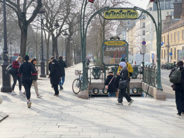Paris,France-15.02.2025 People bustle around an iconic metro entrance in Paris, embracing the vibrant atmosphere of the city on a serene day, framed by winter trees.