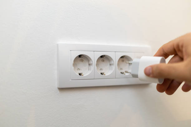 istock Hand Plugging a Smartphone Power Adapter into a Child Proof Wall Electric Socket 2200328772