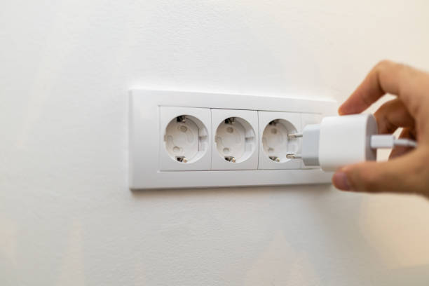 istock Hand Plugging a Smartphone Power Adapter into a Child Proof Wall Electric Socket 2200328785