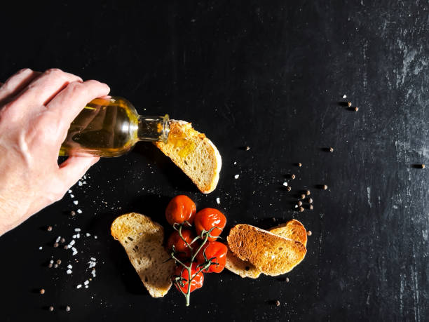 Woman pouring olive oil on toasted bread, decorated with tomatoes and salt on dark table - Concepts and ideas, rustic lifestyle, copy space
