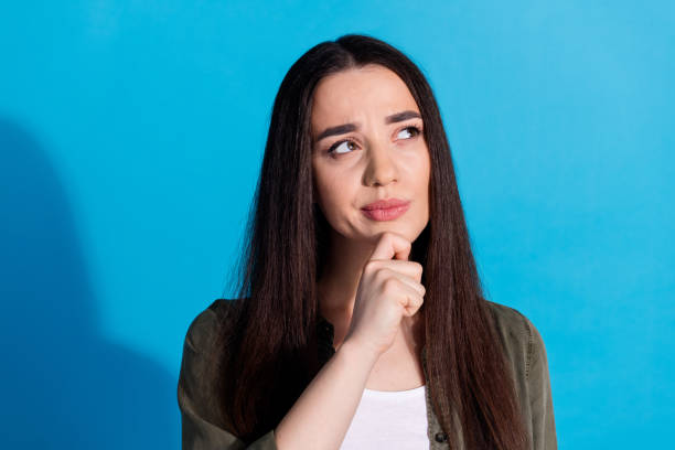 istock Young woman pondering with a thoughtful expression against a vibrant blue background 2200339383