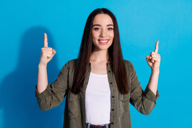 istock Smiling young woman pointing upward with optimism against blue background 2200339411
