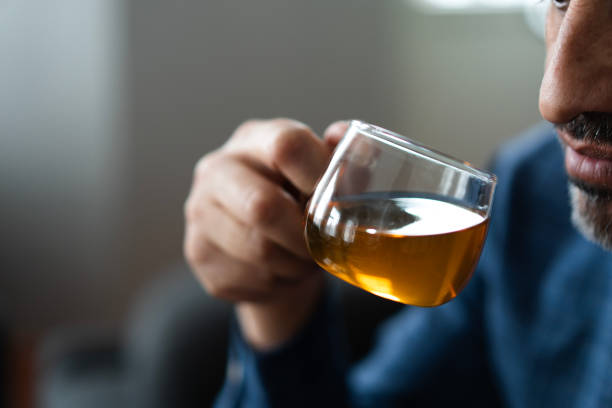 Close up of mature man holding a glass cup of herbal tea, enjoying the aroma and taste